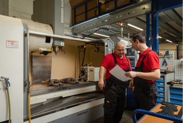 Two men engineers are discussing a blueprint in metal workshop 